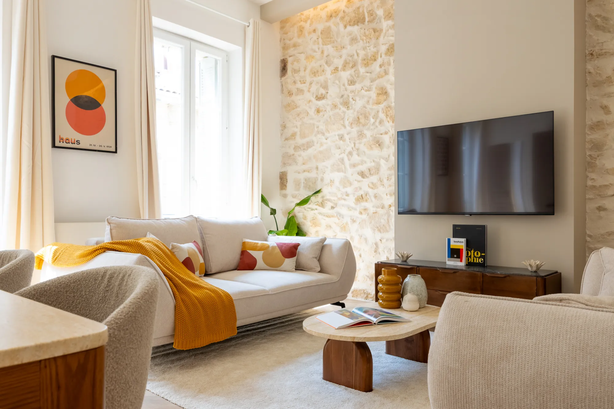 Salon rénové avec mur en pierre, canapé crème et plaid jaune
